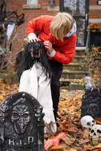 Boy Setting Up Scary Halloween Decorations In Front Yard For Trick-Or-Treat Fright