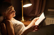 © alfa27 - Beautiful female in pajamas lying on bed reading book, alone at night. Caucasian short haired lady in bedroom, charming cute woman in room lighted by lamp. side view