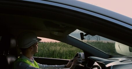 Wall Mural - the power engineer driver rides in the car against the background of high-voltage poles, inspects th