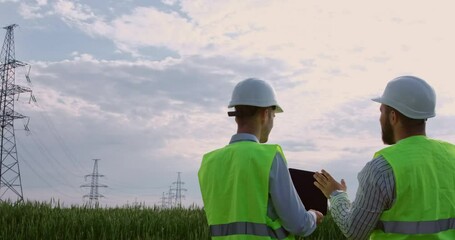 Wall Mural - two power engineers, working with drawings on an electronic tablet, are facing the high-voltage powe