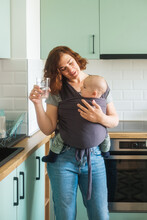 Smiling Woman In The Kitchen Carrying A Baby