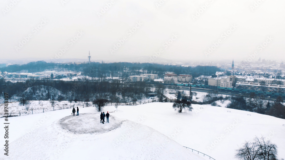 Aerial view of the Krakus Mound (Kopiec Krakusa) also called Krak Mound. A tumulus located in the Podgórze district of Kraków, Poland. Tourists can be seen standing. Whole area covered with snow.  - obrazy, fototapety, plakaty 