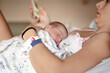 © Albert Martinez/Stocksy - Mother lying in hospital bed with baby sleeping on top of her while using mobile