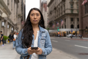 Wall Mural - Young Asian woman in city walking texting cellphone on a street