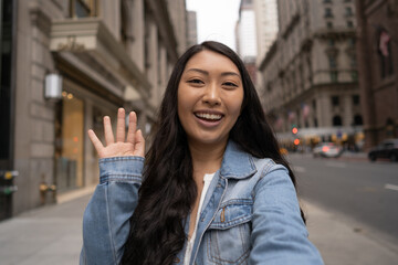 Wall Mural - Young Asian woman in city walking face time video chatting