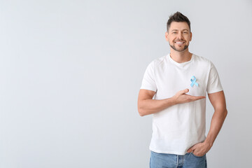 Man with blue ribbon on light background. Prostate cancer awareness concept