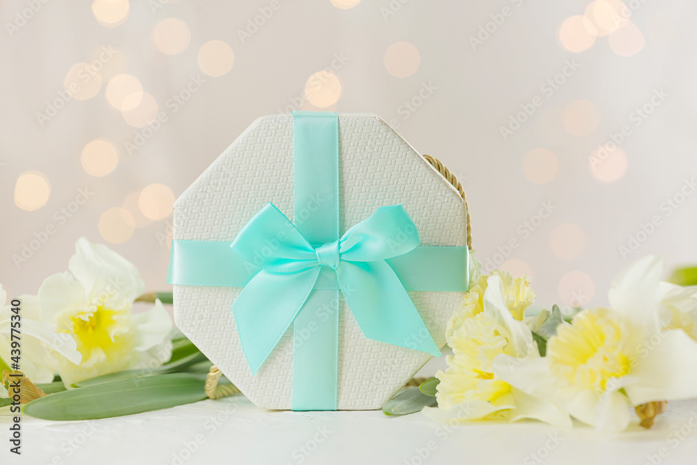 Gift box and beautiful flowers on table against blurred lights