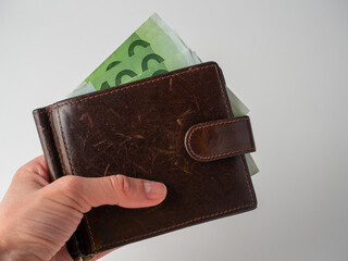 a man's hand holds a brown leather wallet with 100 euro bills sticking out of it on a white background. The concept of money, wealth, wealth