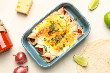 Baking dish with tasty cooked enchilada and ingredients on light background