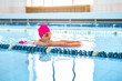 Little kid girl learning to swim with pool board at the public swimming-pool. Space for text