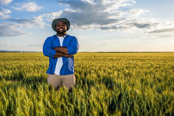 African farmer is standing in his growing wheat field. He is satisfied after successful sowing.