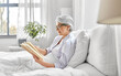 © Syda Productions - old age, leisure and people concept - happy smiling senior woman in glasses reading book in bed at home bedroom
