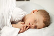 © Aleksandr - The child sleeps sweetly with his fingers to his mouth on a white crib. A little boy has sweet dreams