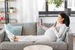 © Syda Productions - pregnancy, rest, people and expectation concept - happy smiling pregnant asian woman sitting on sofa at home having video call on smartphone