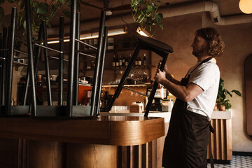 Young white cafe employee in apron working indoors