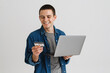 © Drobot Dean - Young man smiling while holding credit card and laptop