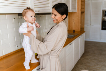 Young mother smiling and playing with her baby in kitchen at home