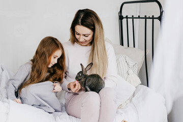 Wall Mural - mom young woman and her little red haired girl daughter sitting in a country house with baby rabbit, summer vibes concept