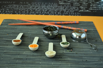 Sticker - Closeup shot of spices on white spoons and chopsticks on a black tablecloth background