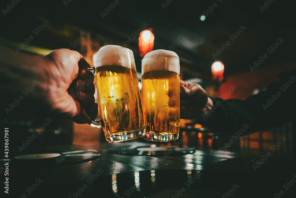 Closeup view of a two glass of beer in hand. Beer glasses clinking in bar or pub - obrazy, fototapety, plakaty 