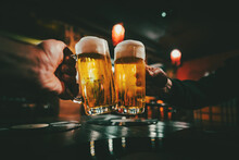 Closeup View Of A Two Glass Of Beer In Hand. Beer Glasses Clinking In Bar Or Pub