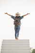 © sutlafk - woman traveler with backpack holding hat, wanderlust travel concept, space for text, atmospheric epic moment. Young adult woman walking up the stairs with sun white  background.