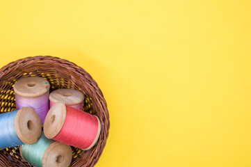 Canvas Print - Basket of colorful sewing threads isolated on a yellow background with free space for text