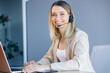© Ivan - Joyful female call center operator in headset looks at the camera, smiling. Smart business woman sits at the table in the office, works in the support service, advises people