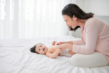 Mother Changing Diaper Of Adorable Baby Girl Lying On Bed,