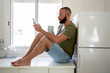 © Eloisa Ramos/Stocksy - Man using his phone at kitchen