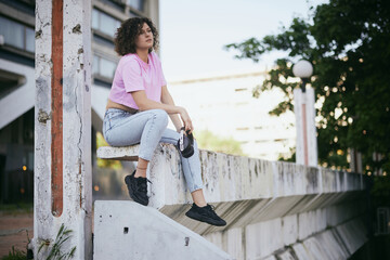 A young attractive woman with curly hair sitting outdoors with headphones in her hands and chilling.