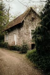 Canvas Print - Vertical shot of an old, stone house surrounded by green trees and plants under a gloomy sky