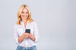 © denis_vermenko - Happy mature senior woman holding smartphone using mobile online apps, smiling old middle aged lady texting sms message chatting on phone looking at cellphone isolated on white grey background