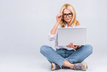 Wall Mural - Business concept. Portrait of happy senior aged woman in casual sitting on floor in lotus position and holding laptop isolated on white background. Copy space for text.