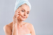 © denis_vermenko - Senior smiling 50s middle aged mature older woman applying facial cream on face looking at camera isolated over white background. Anti age healthy dry skin care beauty therapy concept