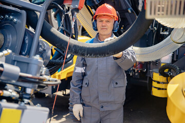 Industrial worker fuel electrician factory in hard hat and headphones monitors electric cable at oil well