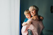 © Olga Moreira/Stocksy - Mother with her little son on her back standing at the window