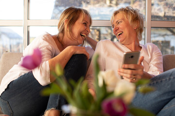 Two ladies 55 years old laughing cheerfully, looking at each other, female friendship concept