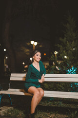 Wall Mural - Vertical shot of a young Caucasian female posing in an elegant green dress sitting on a bench