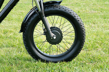 Wheel of the electric bicycle view from side. E bike motor in the park grass of the city. Unfiltered, with natural lighting, urban view. Ecology and green energy concept. Ev – electric vehicle.