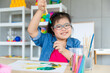 © Bangkok Click Studio - Young Asian down syndrome little girl sitting at desk with colors prepare for painting. She shows brush and widely smiles with bright eyes and happiness. Concept for education for disabled kid
