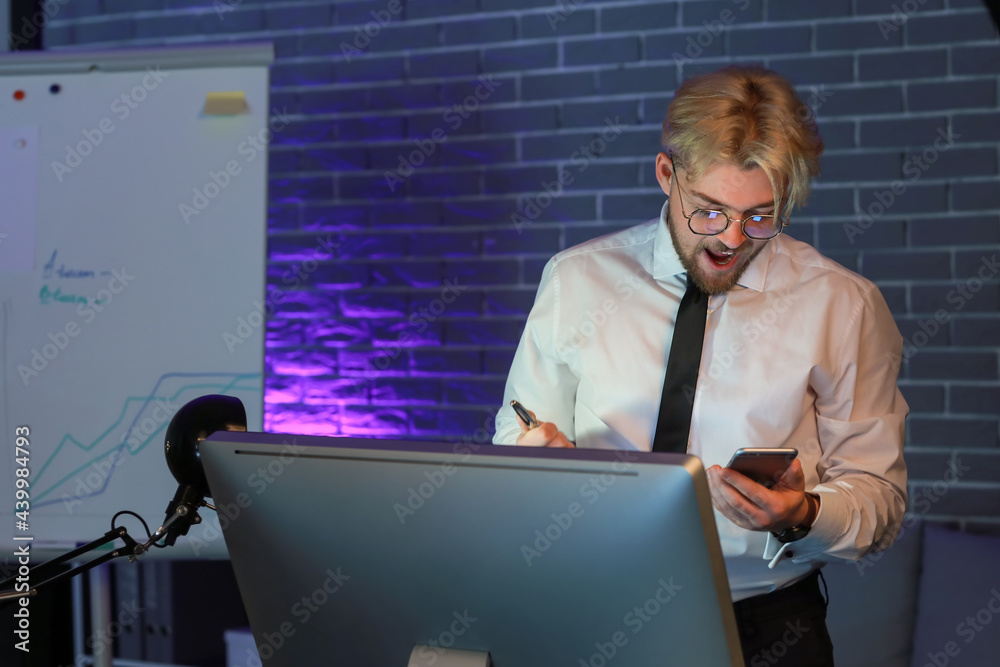 Handsome man with mobile phone in office at night
