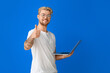 © Pixel-Shot - Handsome man with laptop showing thumb-up on color background