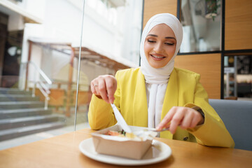 Wall Mural - Young muslim woman in hijab having a lunch in cafe