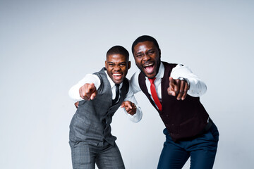 Wall Mural - Two cheerful african american businessmen in shirts and vests laugh and point fingers at the camera