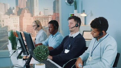 Wall Mural - Multiracial call center agent, bored at work, throwing crumpled paper at his colleague. There are skyscrapers in the background.