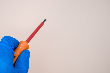 Wall Mural - Closeup of a hand in a blue medical glove holding a screwdriver on the beige background