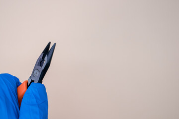 Poster - Closeup of a hand in a blue medical glove holding nippers on the light beige background