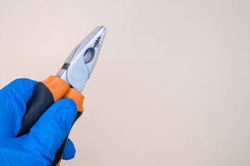 Poster - Closeup of a hand in a blue medical glove holding pliers on the light beige background