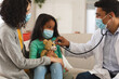 © Wavebreak Media - Hispanic male doctor using stethoscope at home of mother and daughter patient, wearing face masks